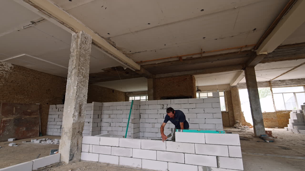 Man building a white brick wall in the spacious old premise with columns. Reconstruction in progress.