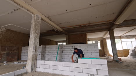 man building a white brick wall in the spacious old premise with columns. reconstruction in progress.