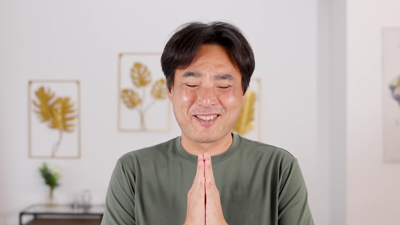 A man in a serene room performs a prayer gesture, conveying gratitude and peace