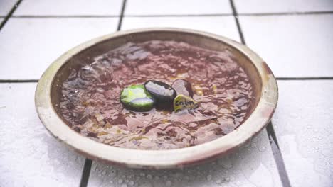 close-up shot of slow-motion rain flooding a red flower clay jar with stacked pebbles and tiled background