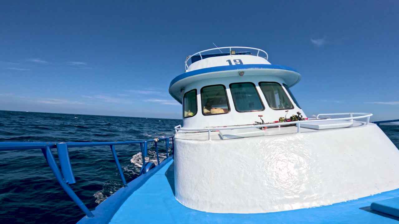 Blue fishing boat cockpit moves through ocean waves under bright daylight, steady forward camera view