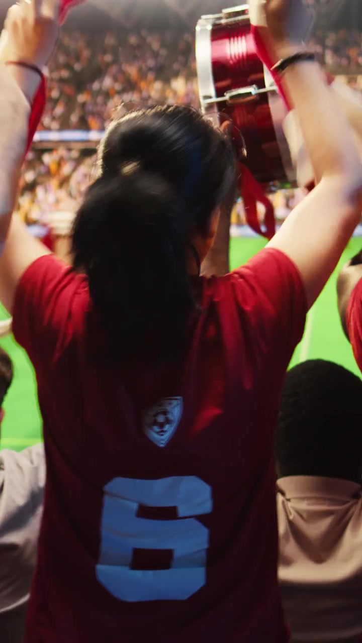 Video vertical. Primer plano de aficionados con camisetas rojas en las gradas del estadio animando.
