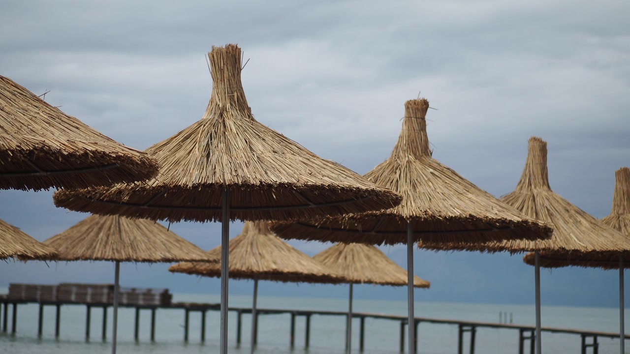 Straw Beach Umbrellas and Pier on a Cloudy Day