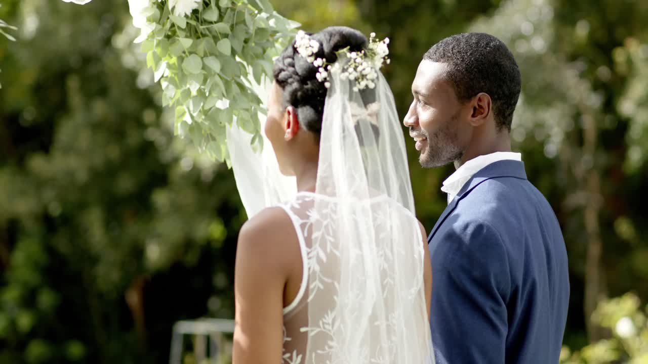 Happy african american couple smiling at their wedding ceremony in sunny garden, in slow motion