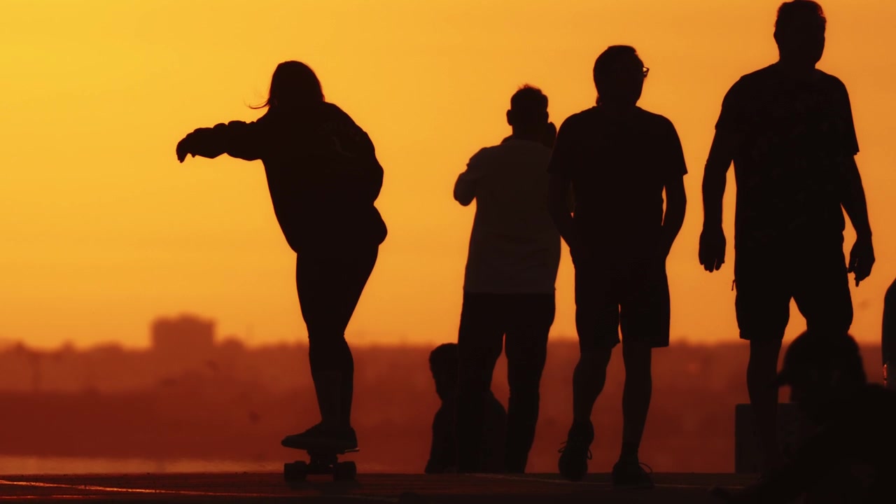 Sagome nere di persone diverse che si divertono in strada contro il luminoso tramonto arancione