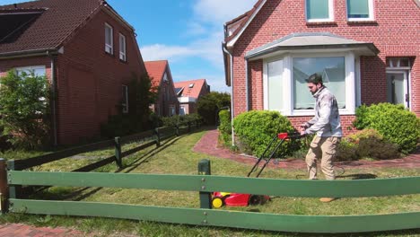 young man cutting the grass with the lawn mower in front of the house next to a fence