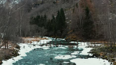 Antena-A-Lo-Largo-De-Un-Río-Congelado-Y-Cruzando-Un-Pequeño-Puente-En-Noruega