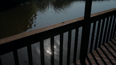 Shadows-of-wooden-railing-reflecting-on-calm-water-under-a-dock