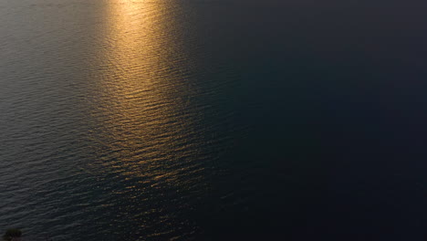 Slow,-aerial,-tilt-shot-revealing-Lake-Garda-at-sunset-with-warm-sunset-light-braking-through-the-clouds-and-spilling-over-the-mountains