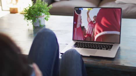 Video-of-woman-sitting-on-sofa-and-watching-football-on-laptop-at-home