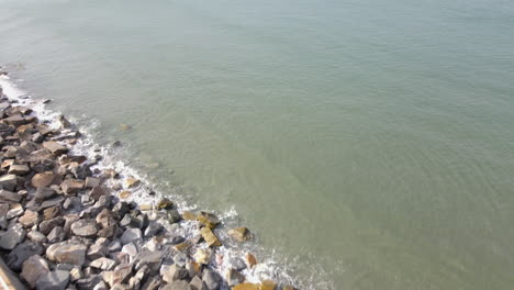 Drone-footage-looking-down-over-parking-lot-and-moving-over-walkway-and-sea-wall-out-to-over-water