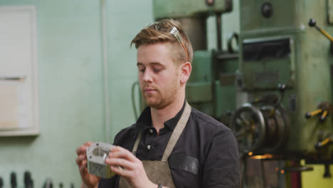 Caucasian-male-factory-worker-at-a-factory-holding-a-metal-part,-looking-and-smiling-to-the-camera