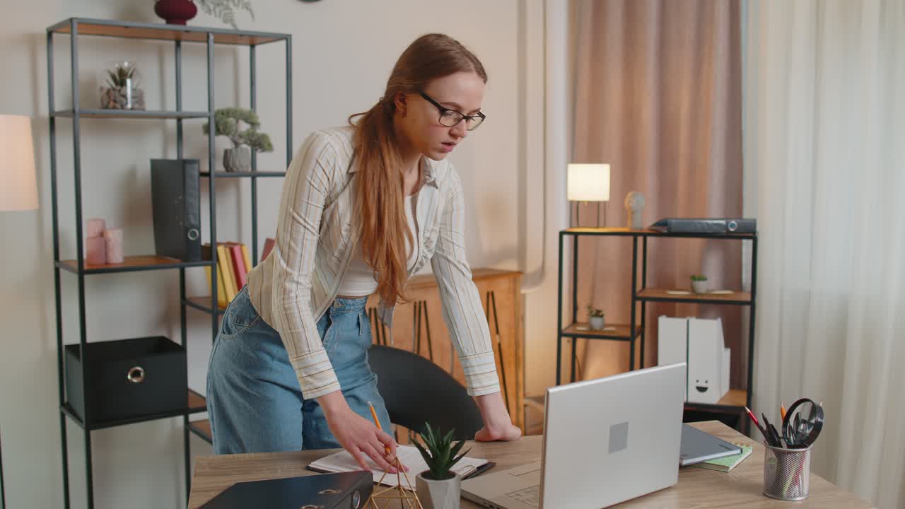 Young woman girl standing by desk in home office working at paper documents analyzes checks data