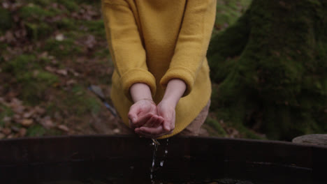 female cups water in hands in nature