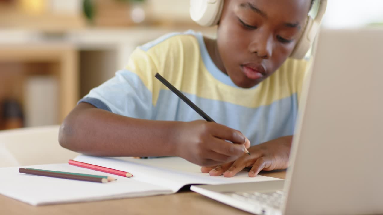 Counting fingertips, African American boy writing homework in notebook with laptop at desk