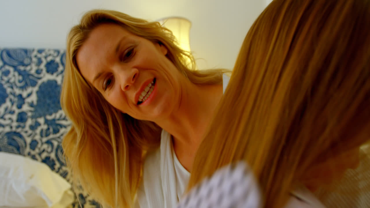 Front view of young Caucasian mother hairdressing her daughters in bedroom of comfortable home 4k