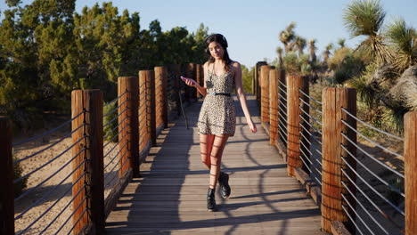 A-beautiful-young-woman-listening-to-music-streaming-from-her-smartphone-on-her-headphones-while-walking-a-bridge-in-nature-SLOW-MOTION