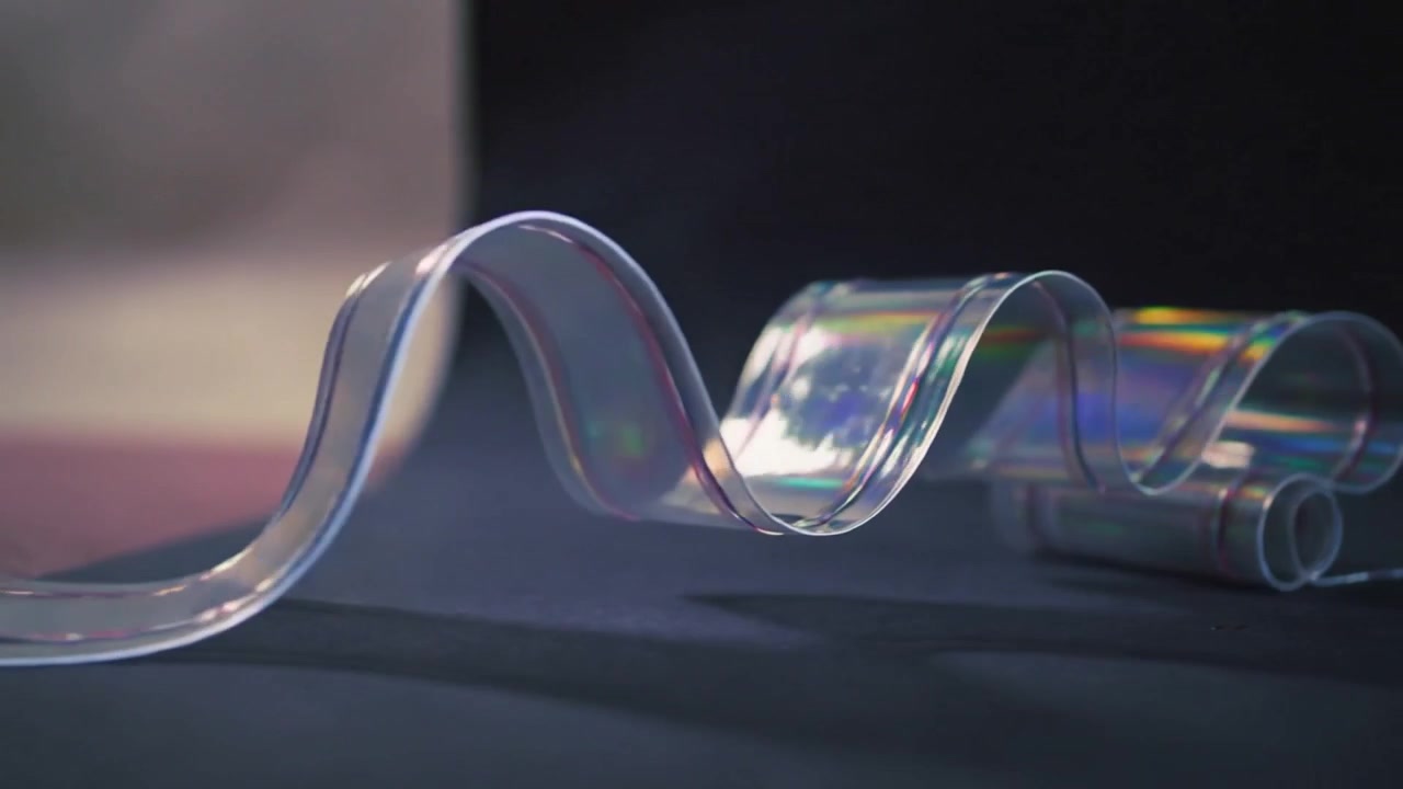 Unfurling clear plastic ribbon making waves and coils on tabletop revealing prismatic highlights