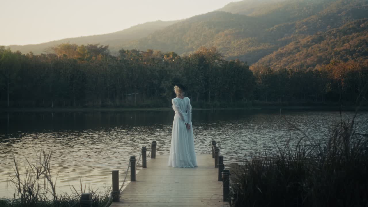 หญิงสาวสง่างามในชุดสีขาวยืนอยู่บนท่าเทียบเรือยามพระอาทิตย์ตกดิน