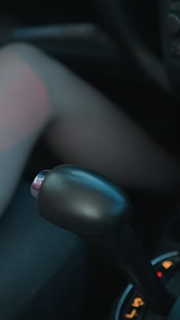 mujer en vestido rosa sentada en su coche coloca cuidadosamente la taza de café cerca del cambio de marchas, el interior del coche está ligeramente borroso, y las sombras de los vehículos que pasan crean un brillo suave en ella