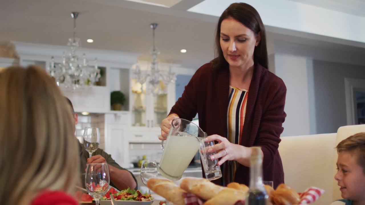 madre caucásica sonriente vertiendo limonada para los niños en la mesa antes de la comida familiar