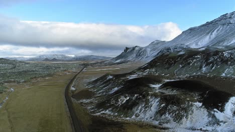 A-dirt-road-by-the-snow-covered-mountains-of-Iceland---aerial