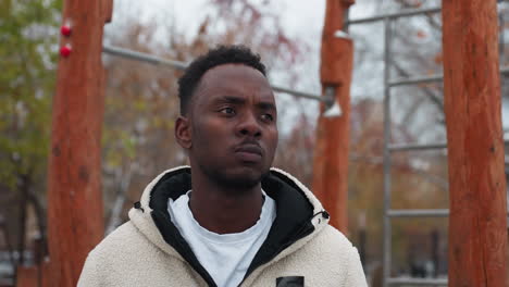 remote worker standing outdoors in winter, staring into distance with a frown, dressed in warm fleece jacket, surrounded by workout equipment, leafless trees, and light snow on ground