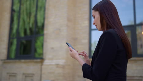 businesswoman scrolling mobile phone outdoor. people walking street with devices