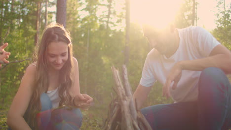 a couple man and a woman together collect a fire from sticks in the woods. a young couple in a hike puts a fire for the night and cooking in nature