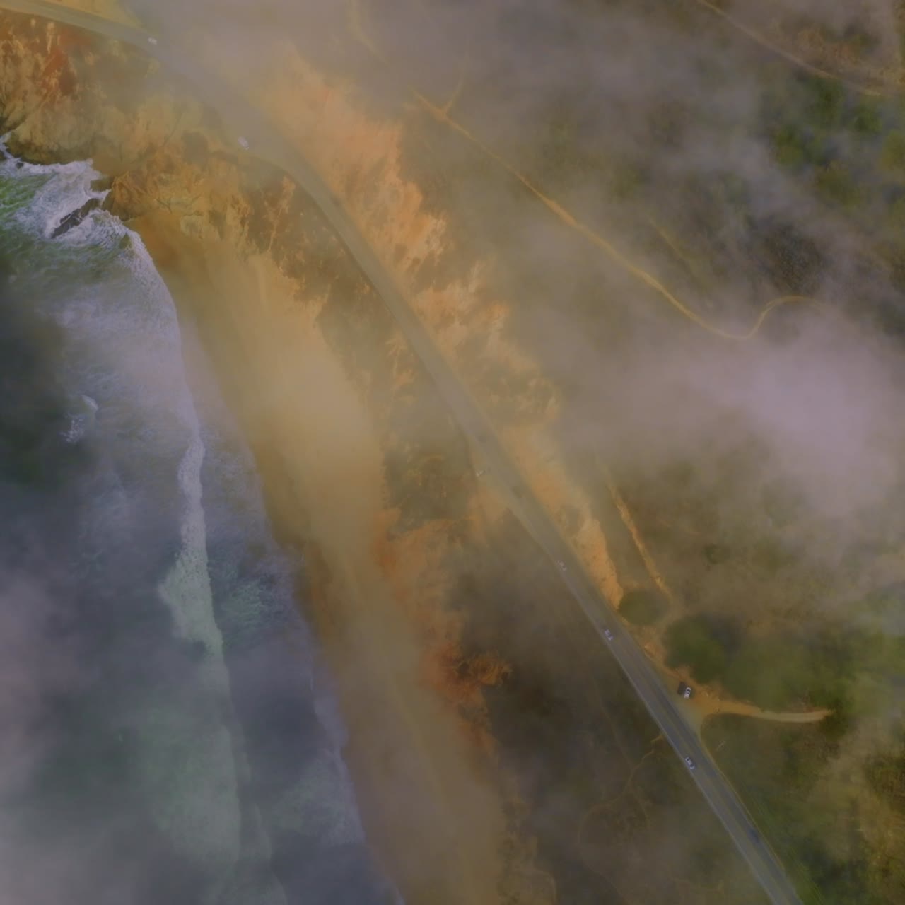 Rocky beach with waves coming back and forth. Highway with cars moving by in the mountains. Amazing scenery covered with fog in Montara, California, USA
