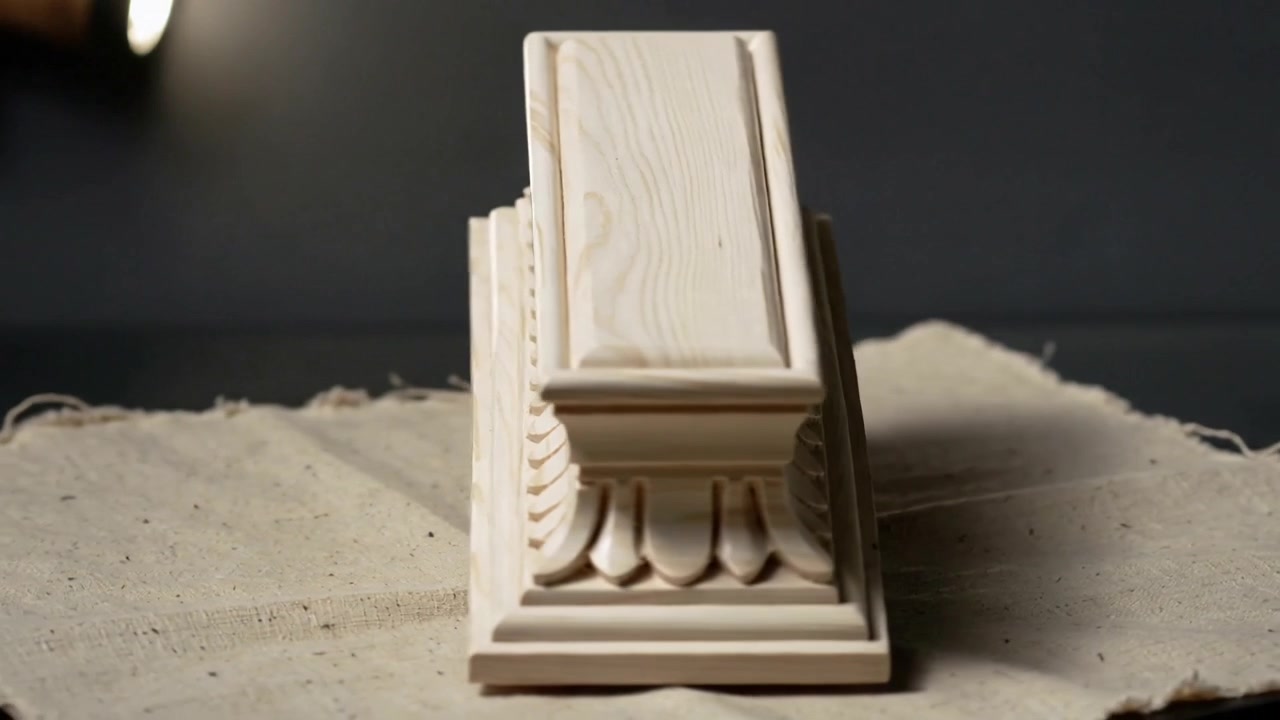 Piattaforma girevole che ruota una modanatura in legno intagliato su un tavolo da studio con panno beige e luce soffusa