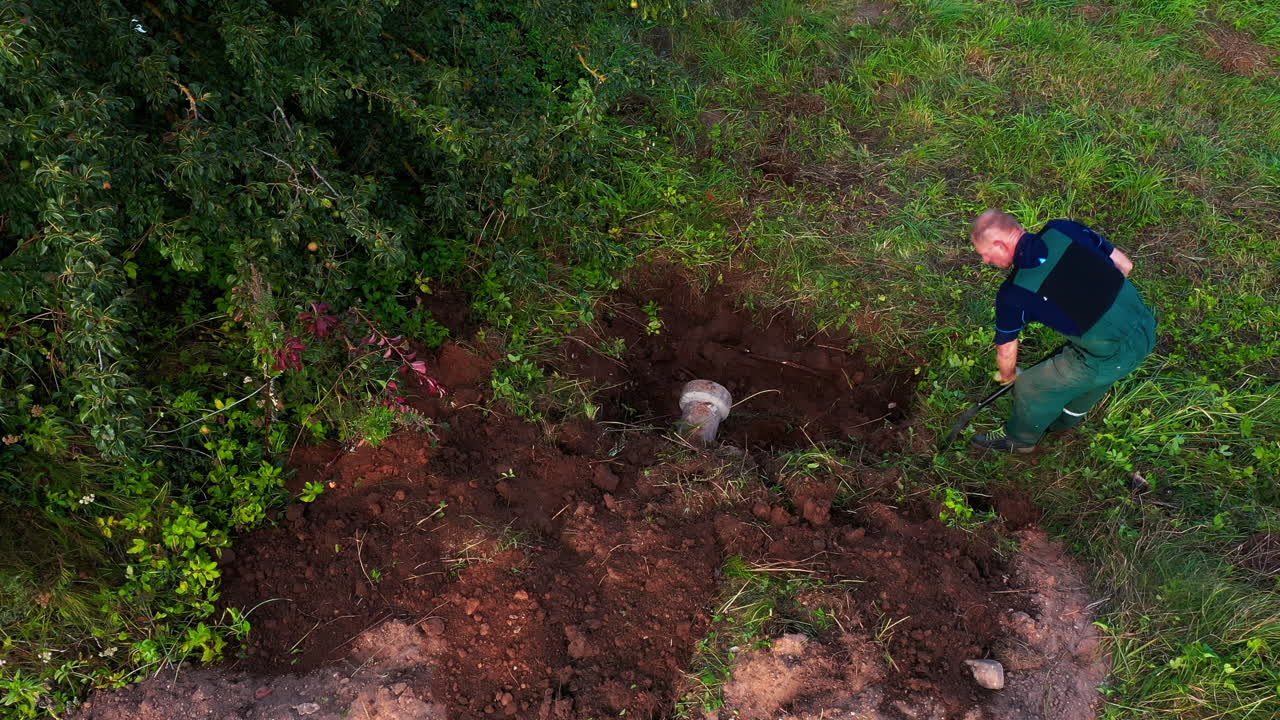 Elder man in 50s working with shovel in yard, digging hole for smokehouse foundation
