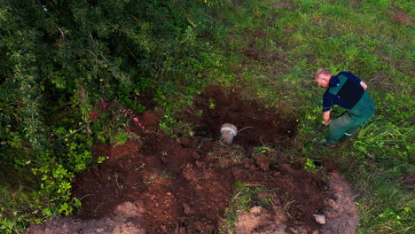 elder man in 50s working with shovel in yard, digging hole for smokehouse foundation