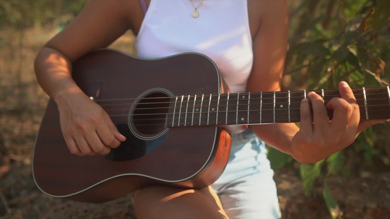 primer plano de la mano y la guitarra de una chica tocando al aire libre mientras el sol brilla en su cuerpo