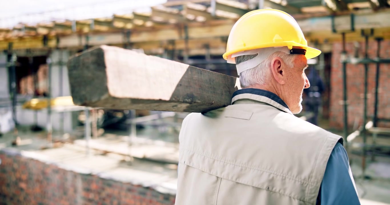 Senior Construction Worker Carrying Wooden Beam on Shoulder at Building Site