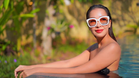 Woman-inside-pool-leaning-on-the-edge-of-the-pool-and-looking-aside,-slow-motion-face-close-up