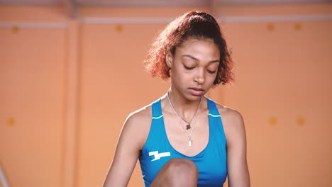 portrait of a focused young sportswoman stretching legs and looking at camera in an indoor sport facility