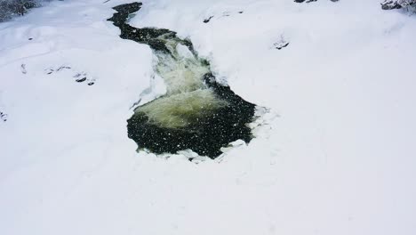 flying down and tilting up on a small water fall on a frozen river during a snow storm slow motion aerial