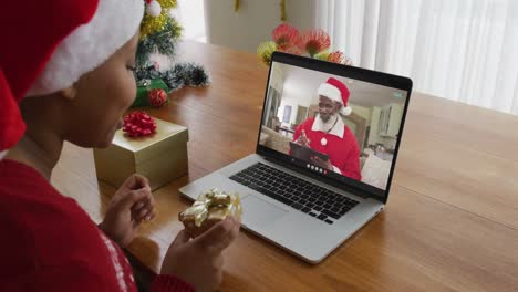 Afroamerikanische-Frau-Mit-Weihnachtsmütze-Nutzt-Laptop-Für-Einen-Weihnachtsvideoanruf-Mit-Dem-Weihnachtsmann-Auf-Dem-Bildschirm