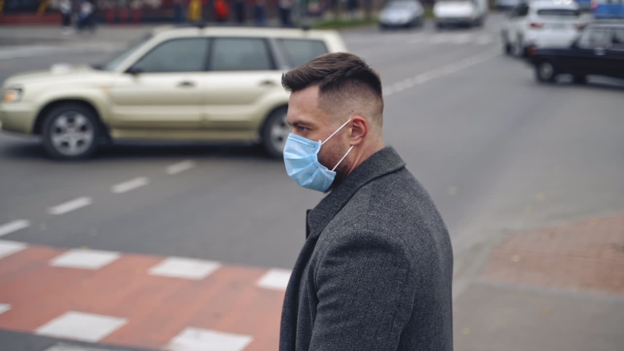Man in medical mask outdoors. Young male wearing protective coronavirus mask on city street and looking around. N1H1 coronavirus. Slow motion.