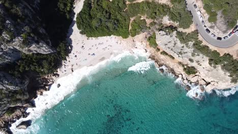 Drohne-Erhebt-Sich-Und-Schwenkt-Mit-Einem-Katamaran-In-Kristallklarem-Wasser-Und-Ein-Paar-Wellen-über-Die-Berühmte-Bucht-Cala-Fuili-Auf-Sardinien