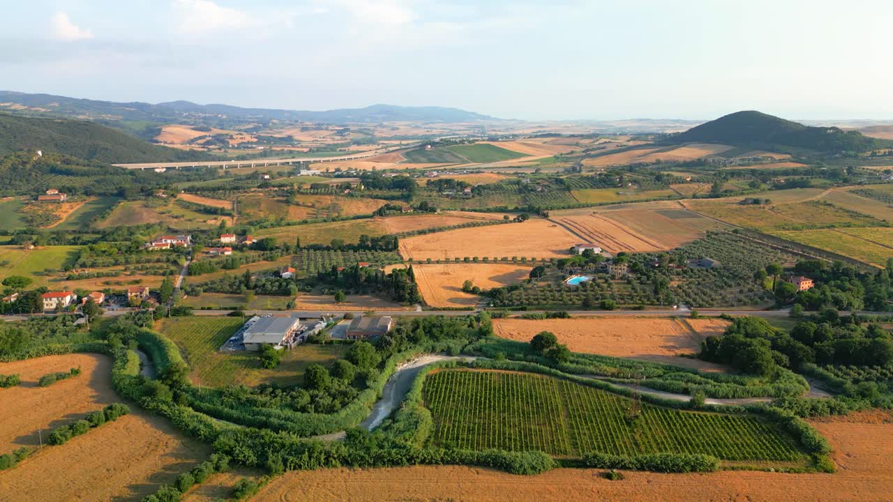 Golden sunlight bathes the picturesque landscape of tuscany, italy, highlighting vineyards, cultivated fields, and a meandering river flowing through the valley