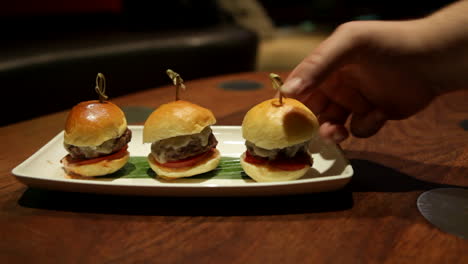 a tray of delicious beef sliders is served at a restaurant as a male customer grabs a slider to eat