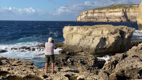 unidentifiable older man photographs the coast of gozo, malta- blue hole, dwejra