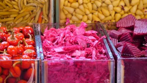 a vibrant display of colorful pickled vegetables, featuring red peppers, pink cabbage, and purple beets at a market stall