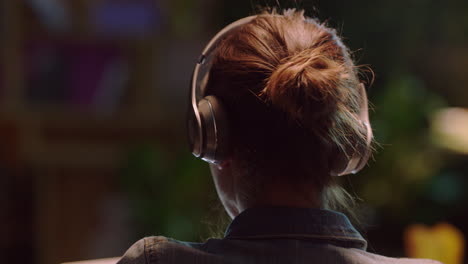 rear view young business woman working late using laptop computer browsing online planning creative startup strategy listening to music wearing headphones in office at night