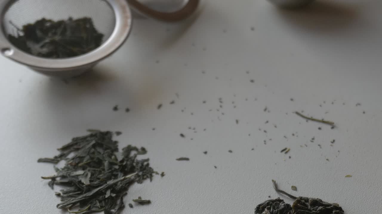 A close-up of green tea leaves scattered on a surface, some leaves in a container nearby