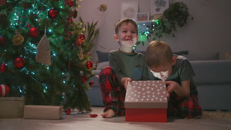 two boys together open a christmas present under the tree. light from a gift. high quality 4k footage