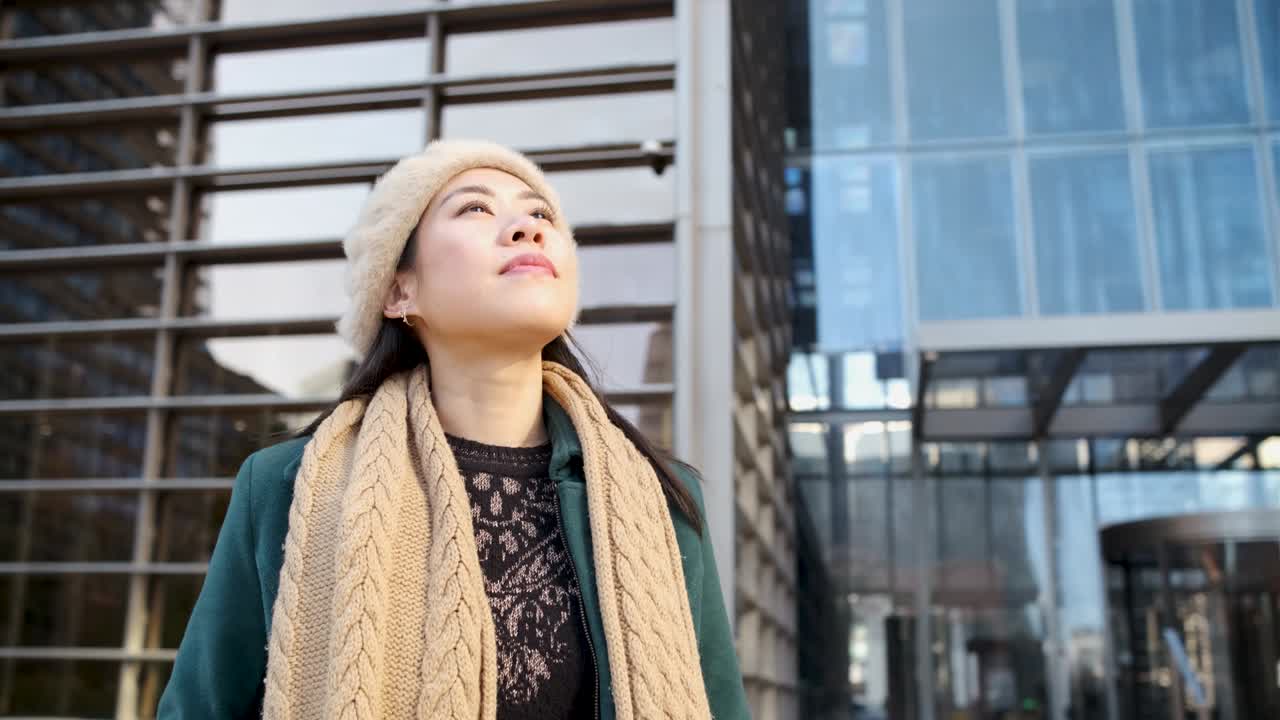 자신감 넘치는 아시아 여성이 금융시티 지역의 거리에서 야외에 서있는 동안 멀리보고 있습니다.