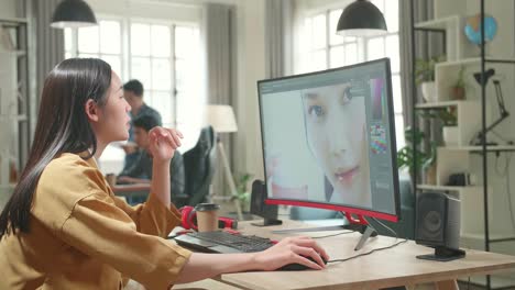 asian female digital editor thinking while works in photo editing software on her personal computer with big display in office